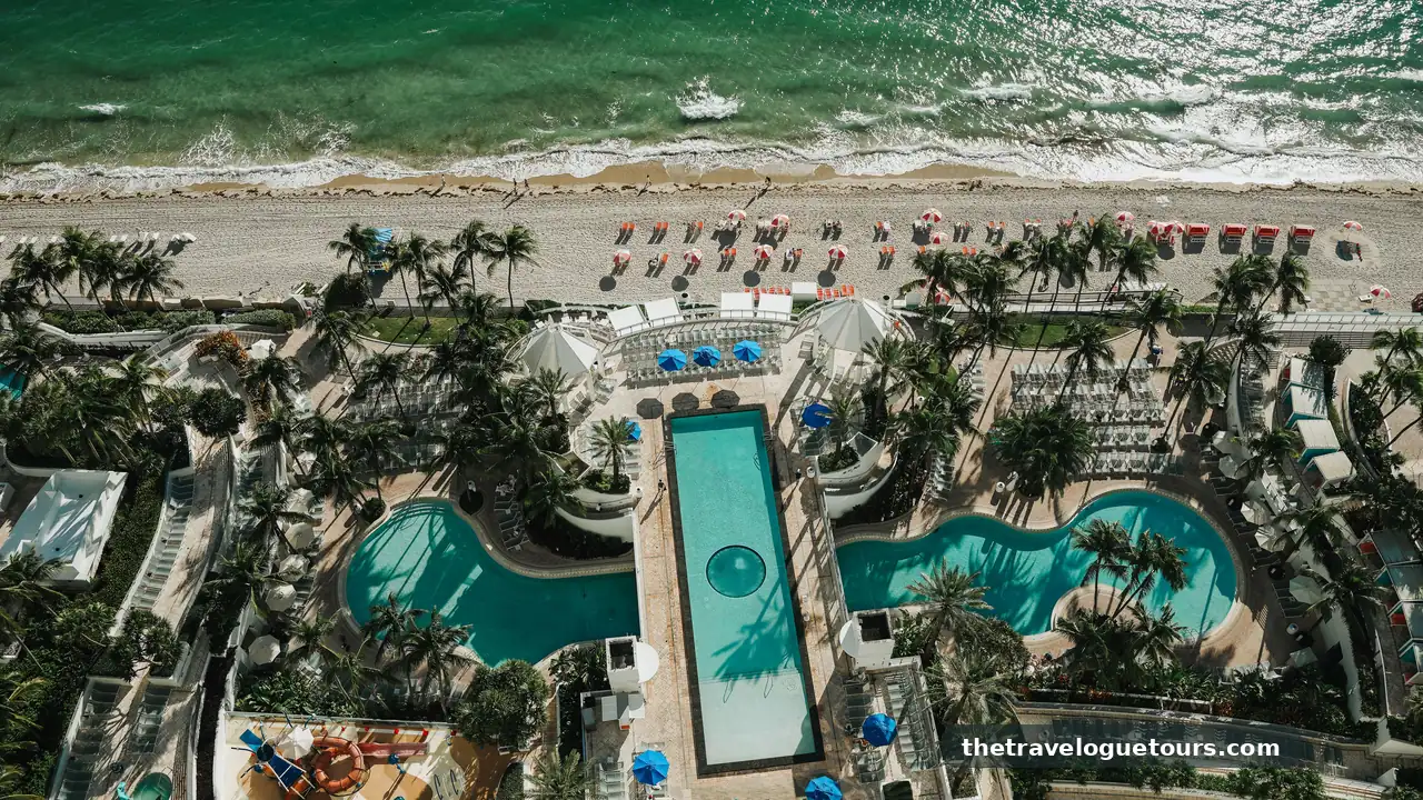 Aerial view of a beachfront Miami resort with pools, palm trees and turquoise sea